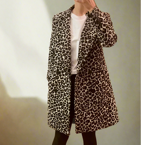 Person wearing a leopard print coat in a room with wooden flooring and a door.