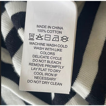 Load image into Gallery viewer, Clothing label with washing instructions on a striped fabric background