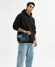 Load image into Gallery viewer, Person wearing a black shirt and blue jeans holding a patchwork bag on a white background