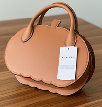 Load image into Gallery viewer, Brown leather handbag with a Coach tag on a gray surface