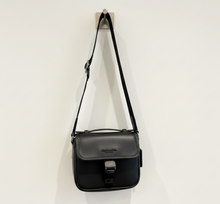 Load image into Gallery viewer, Black Coach handbag held in a store setting with other bags in the background.