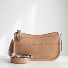 Load image into Gallery viewer, A Coach shoulder bag in tan crocodile-embossed leather, displayed on a white faux fur surface against a dark gray background, with its matching strap and a white COACH card in front.