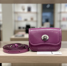 Load image into Gallery viewer, A purple patent leather belt bag with a silver-tone turn-lock closure, shown next to its matching purple leather belt on a white faux fur background.