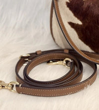 Load image into Gallery viewer, A brown leather shoulder strap with gold-tone hardware and white contrast stitching, displayed on a white faux fur surface next to a brown and white cowhide bag.