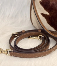 Load image into Gallery viewer, A brown leather shoulder strap with gold-tone hardware and white contrast stitching, displayed on a white faux fur surface next to a brown and white cowhide bag.