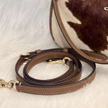 Load image into Gallery viewer, A brown leather shoulder strap with gold-tone hardware and white contrast stitching, displayed on a white faux fur surface next to a brown and white cowhide bag.