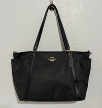 Load image into Gallery viewer, Black Coach handbag held by a person against a light background