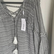 Load image into Gallery viewer, Black and white striped shirt with tassels on a hanger against a white background