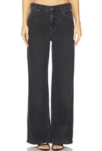 Load image into Gallery viewer, A model wearing a pair of wide-leg black denim jeans with a faded wash, paired with black strappy sandals, shown from the waist down on a white background.