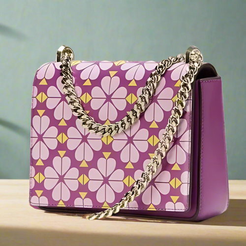 Purple handbag with floral pattern and gold chain strap on a light pink background