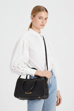 Load image into Gallery viewer, Woman holding a black handbag against a white background