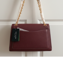 Load image into Gallery viewer, Maroon handbag with a visible tag on a white door