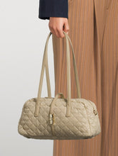 Load image into Gallery viewer, Beige quilted handbag held by a person wearing a dark coat and brown pants.