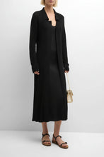 Load image into Gallery viewer, A woman modeling a long, open-front cream-colored knit cardigan over a matching cream dress, styled with brown strappy sandals and a small woven handbag against a plain white studio background.
