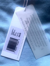 Load image into Gallery viewer, Clothing tag with brand name and price on a blue fabric background