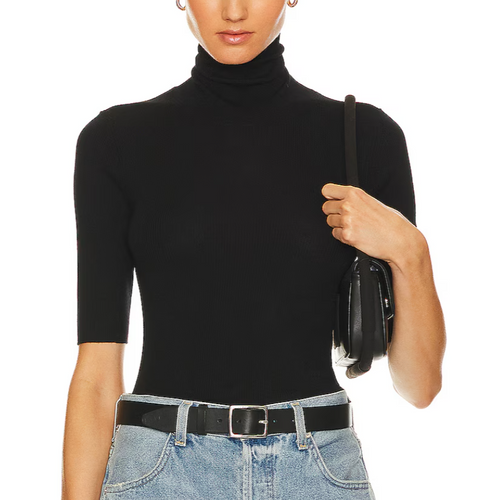 Person wearing a black turtleneck sweater and blue jeans, holding a black handbag on a white background