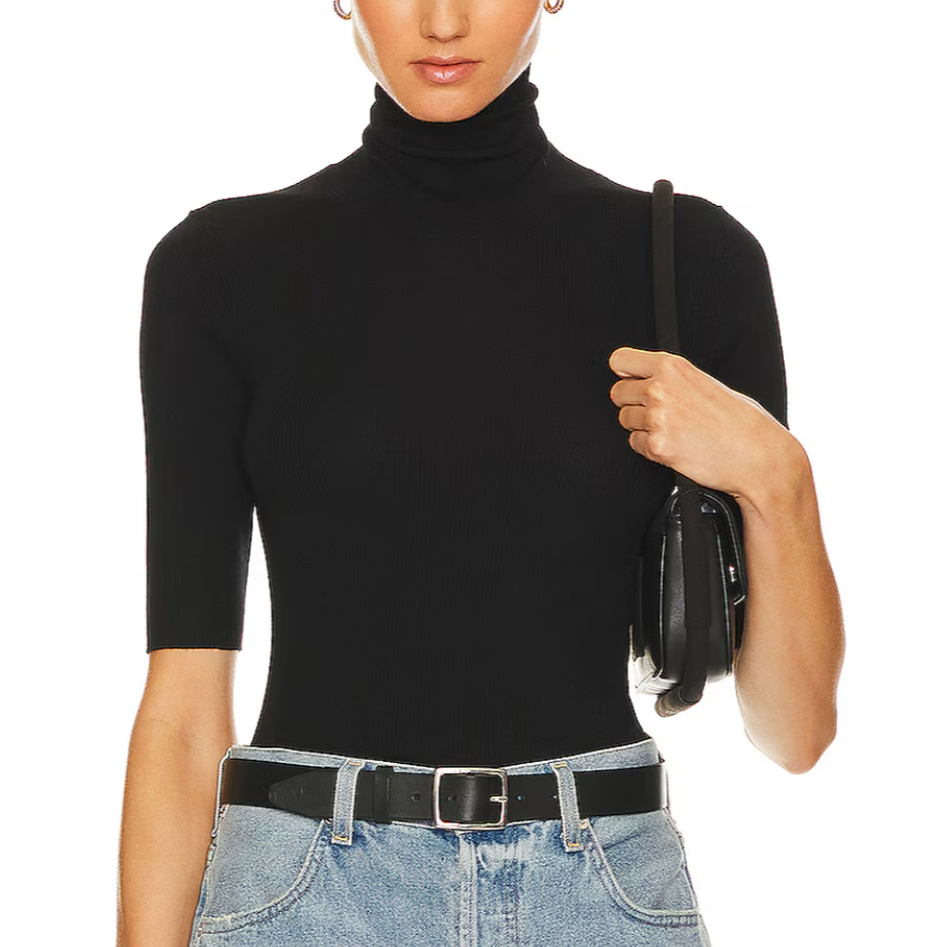 Person wearing a black turtleneck sweater and blue jeans, holding a black handbag on a white background